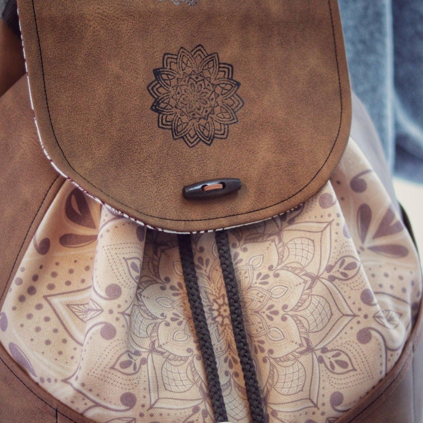 Rucksack aus braunem Kunstleder, Detailansicht. Vorne aus Stoff mit dezentem Mandala von AnyArtDesign