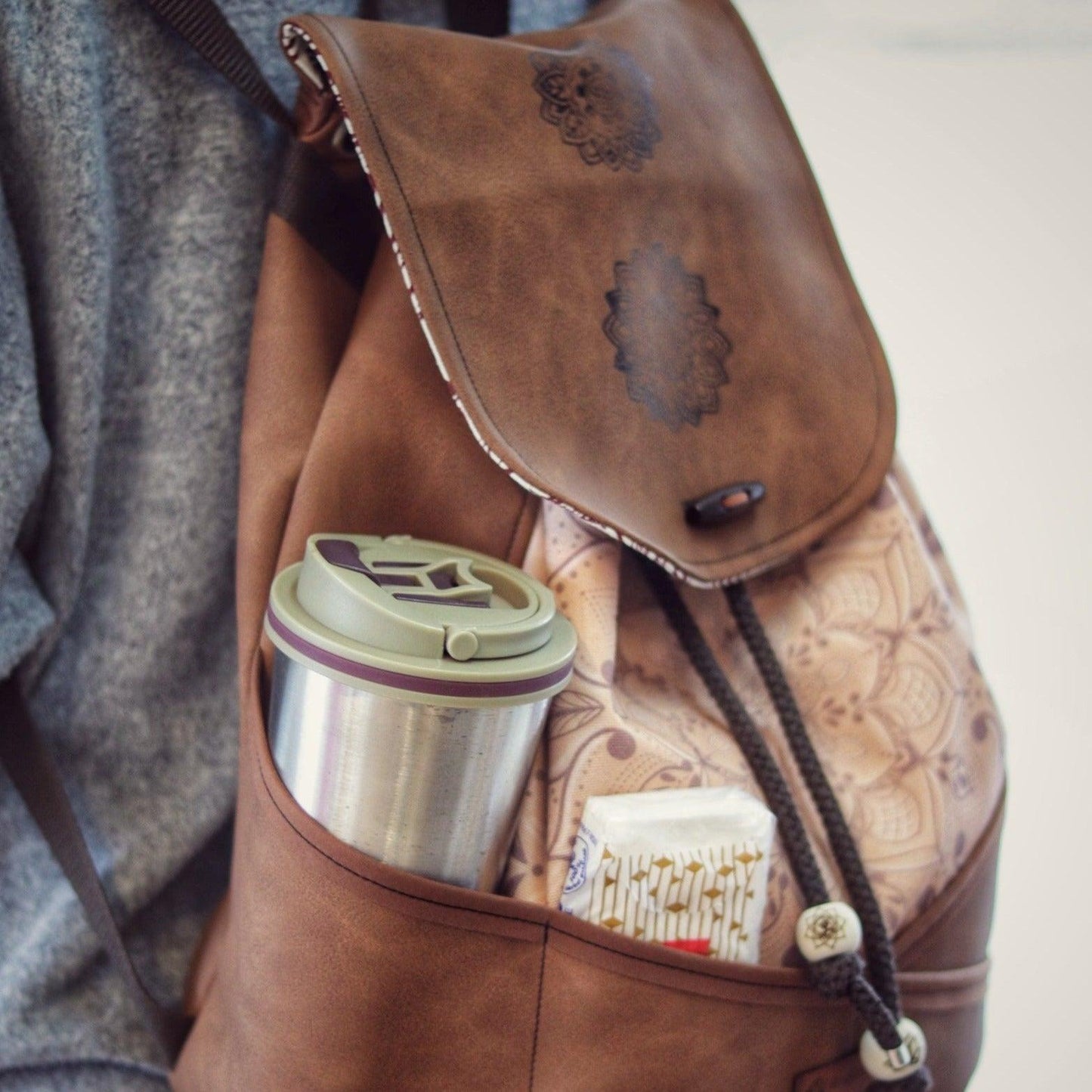 Rucksack aus braunem Kunstleder, Seitenansicht mit Steckfächern. Vorne aus Stoff mit dezentem Mandala von AnyArtDesign